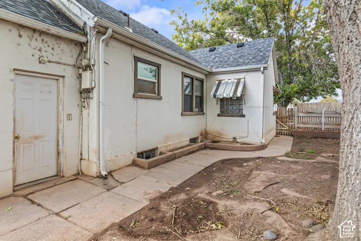 Exterior features include a white stucco facade, shingled roofing, a paved walkway, built-in concrete planters, and a wooden privacy fence