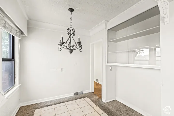 Built-in wall cabinetry with glass-front sliding doors, ornate metal chandelier, crown molding, and tiled flooring