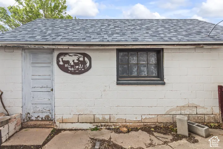 Exterior structure featuring painted concrete block walls, a multi-pane window with dark trim, an entry door, and a gabled roof with asphalt shingles