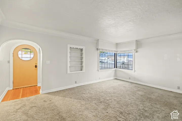 Arched entryway featuring a round-window door, recessed wall shelving, neutral carpet flooring, and a multi-pane corner window