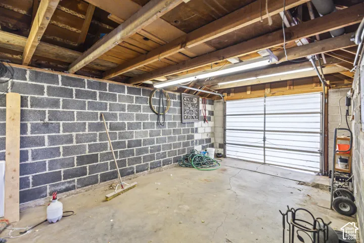 Enclosed garage featuring exposed structural wood ceiling beams, concrete block walls, a concrete floor, and overhead fluorescent lighting