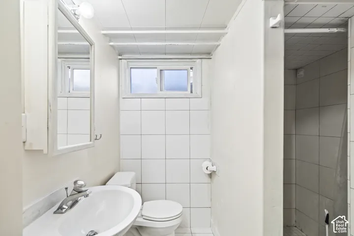 Bathroom featuring a wall-mounted medicine cabinet, white pedestal sink, tiled wall accents, and a walk-in shower enclosure