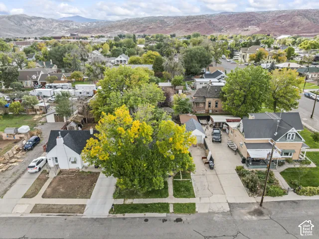 Aerial perspective of the property featuring a detached garage, mature canopy trees, concrete driveway, and expansive mountain scenery
