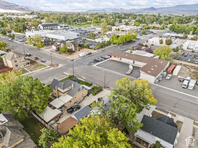 Aerial perspective of residential property featuring mature trees, off-street parking, and mountain terrain backdrop