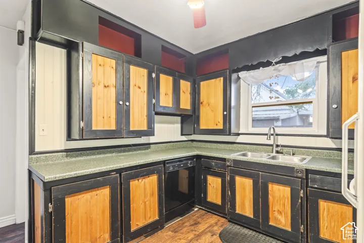 Kitchen featuring two-tone cabinetry with wood-finish panels, solid surface countertops, a stainless steel dual-basin undermount sink, and wood-finish flooring