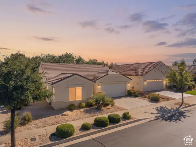 Stucco exterior residence featuring a tile roof, an attached garage, and xeriscaped front grounds with mature ornamental shrubbery