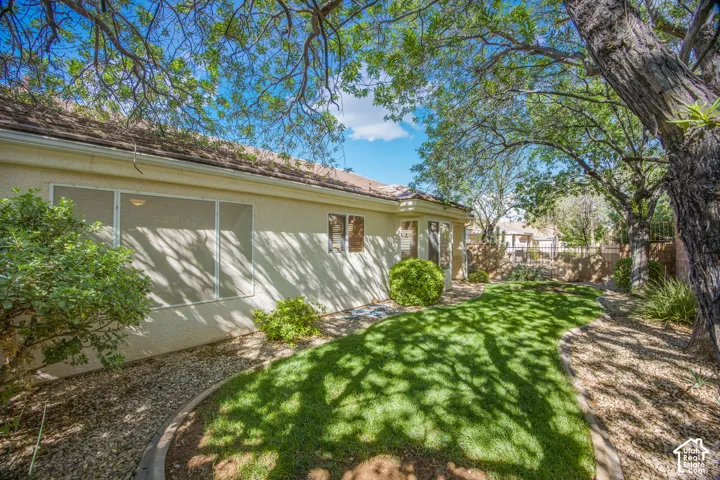 Rear yard featuring a manicured lawn, stone ground cover, perimeter masonry wall, mature trees, and stucco exterior finish