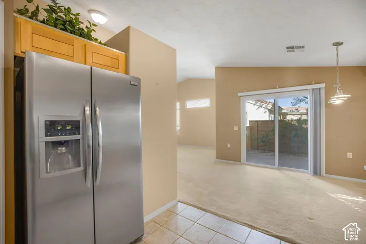 Stainless steel side-by-side refrigerator, light-toned cabinetry, neutral-toned tile flooring, sliding glass door, and pendant lighting