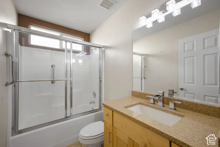 Bathroom featuring a vanity with a light wood finish and stone countertop, an integrated rectangular sink, a chrome faucet, and a shower-tub combination with sliding glass doors