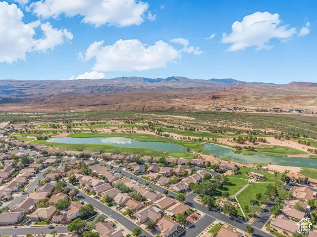 Aerial perspective showcasing an expansive residential community featuring a prominent lake, a sprawling golf course, and a backdrop of mountain terrain