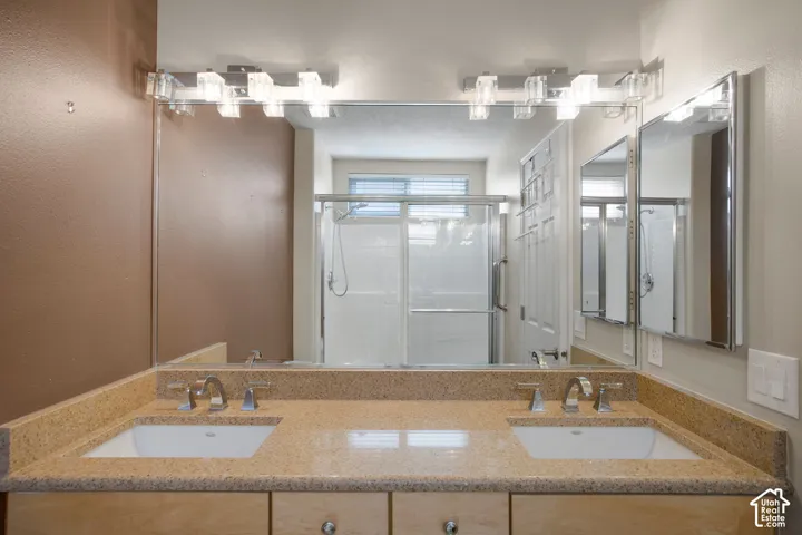 Double vanity featuring a stone-composite countertop, dual undermount sinks, polished chrome widespread faucets, and a full-width mirror with dual multi-bulb light fixtures
