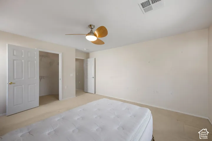 Neutral-toned interior featuring carpeting, a multi-blade ceiling fan with integrated lighting, and a reach-in closet with built-in wire shelving