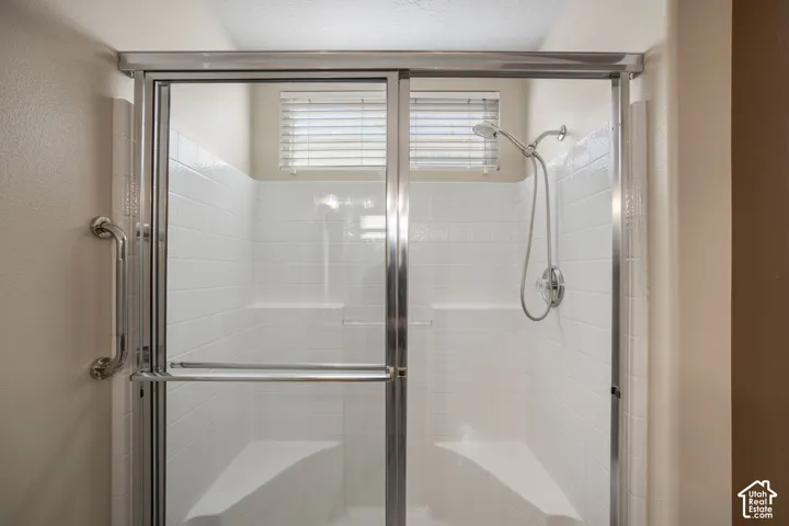 Shower enclosure featuring white tile surrounds, built-in corner seating, a chrome handheld shower head, and a sliding glass door