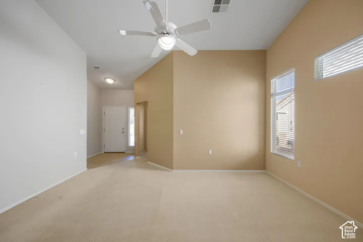 Vaulted ceilings, neutral carpeting, ceiling fan with integrated lighting, and multiple windows with horizontal blinds