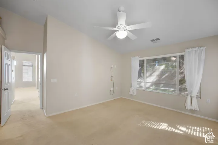 Vaulted ceilings, neutral carpeting, large windows, and a central ceiling fan