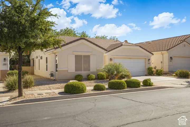 Stucco exterior residence featuring a tile roof, an attached two-car garage, and xeriscaped landscaping with manicured shrubs