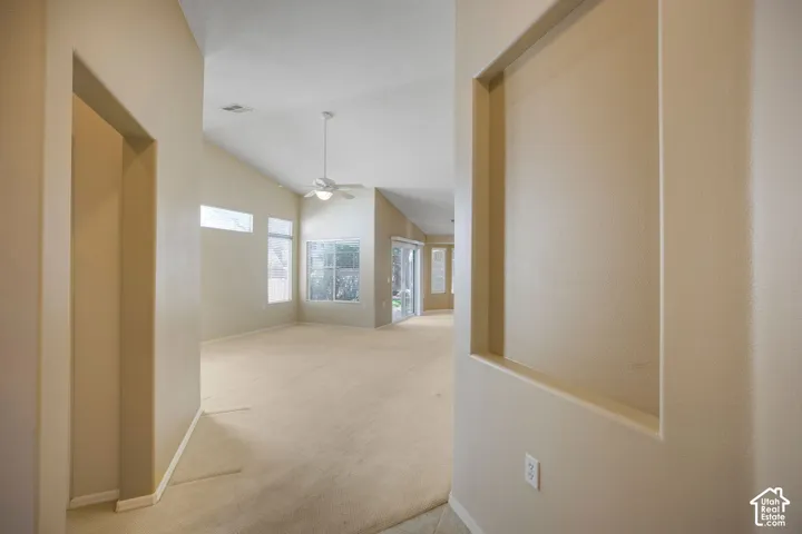 Vaulted ceilings, built-in wall niche, neutral carpeting, multiple windows, and a ceiling-mounted light fixture