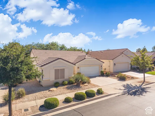 Single-story residence featuring a stucco exterior, concrete tile roof, attached two-car garage, and xeriscaped front yard with mature shrubs