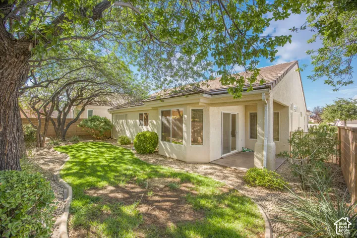 Stucco exterior featuring a covered patio, a grass lawn, mature trees, and rock landscaping