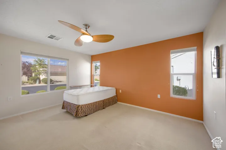 Neutral carpeted flooring, three-blade ceiling fan with integrated lighting, accent wall, and multiple windows providing natural light
