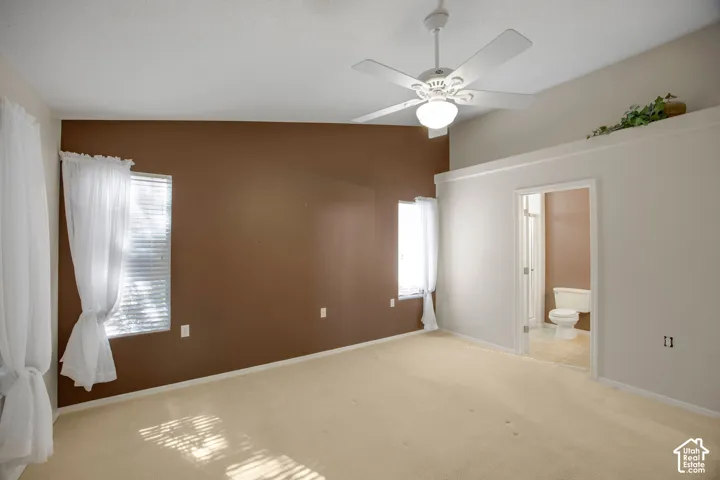 Vaulted ceilings, carpeted flooring, two dual-pane windows, and a ceiling-mounted light fixture with fan, featuring an entry to a tiled room with a commode