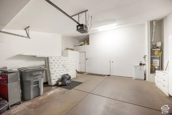 Multi-car garage featuring a concrete floor, high ceilings, built-in wall shelving, an integrated water heater, and an automatic door opener