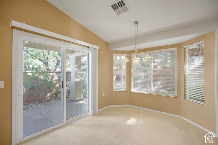 Vaulted ceilings, bay window configuration, sliding glass door, and multi-light pendant fixture