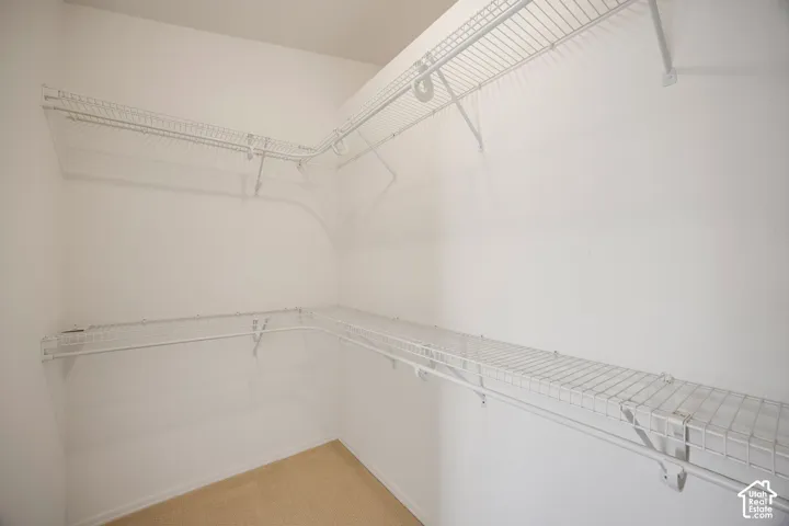 Walk-in storage space featuring multi-level white wire shelving and neutral carpeted flooring