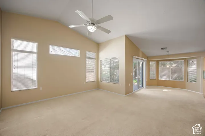 Vaulted ceilings featuring a central overhead fan, abundant natural light from multiple windows, horizontal blinds, and sliding glass exterior doors