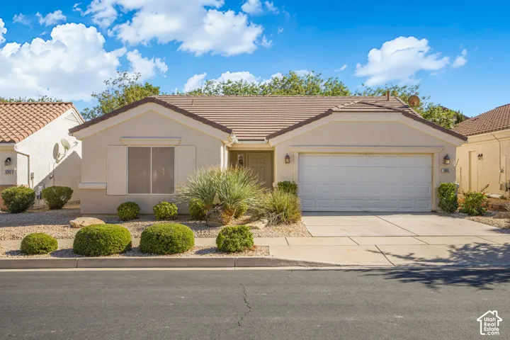 Single-story stucco exterior featuring a concrete tile roof, two-car garage, and xeriscaped front yard with integrated shrubbery