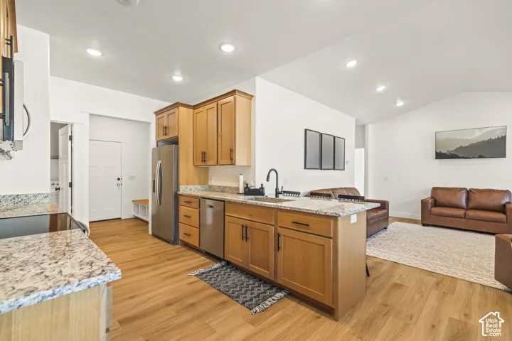 Kitchen featuring light wood cabinetry, stone countertops, stainless steel appliances, a matte black faucet, and wood-finish flooring