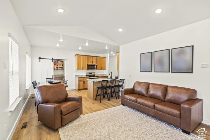 Vaulted ceilings featuring recessed lighting, wood-finish flooring, kitchen island with stone-surface countertop, and pantry with sliding barn-style door