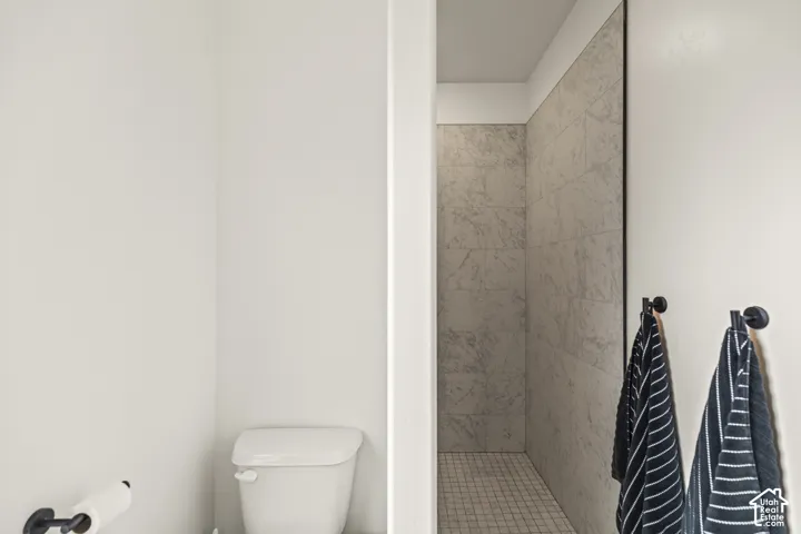 Walk-in shower featuring floor-to-ceiling stone-pattern tile surround, square mosaic tile flooring, and matte black hardware