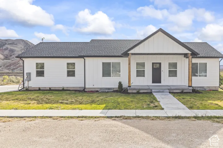 Single-story residence featuring a white vertical board-and-batten and horizontal siding exterior, gable roofline, covered front porch with timber support posts, and a concrete walkway