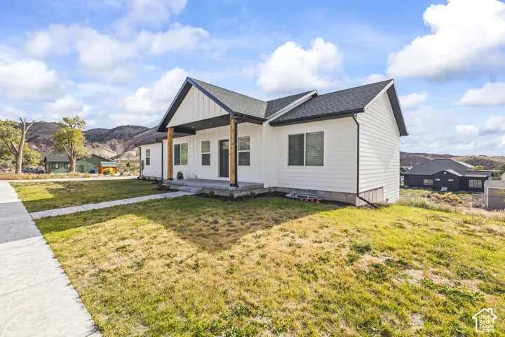 Modern farmhouse exterior featuring white board-and-batten siding, natural wood support columns, a covered front porch, and a mountain backdrop