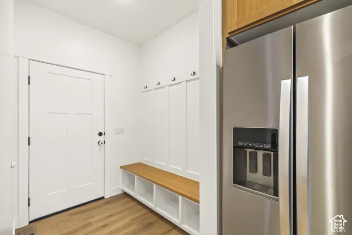 Built-in mudroom bench with integrated storage cubbies, wall-mounted coat hooks, paneled wainscoting, wood-finish flooring, and stainless steel refrigerator
