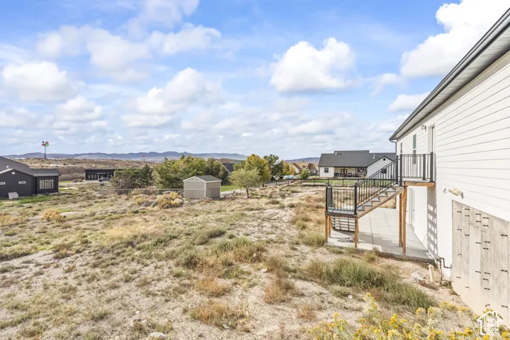Exterior featuring horizontal siding, elevated deck with metal railing, concrete patio, and detached storage structure on an expansive lot