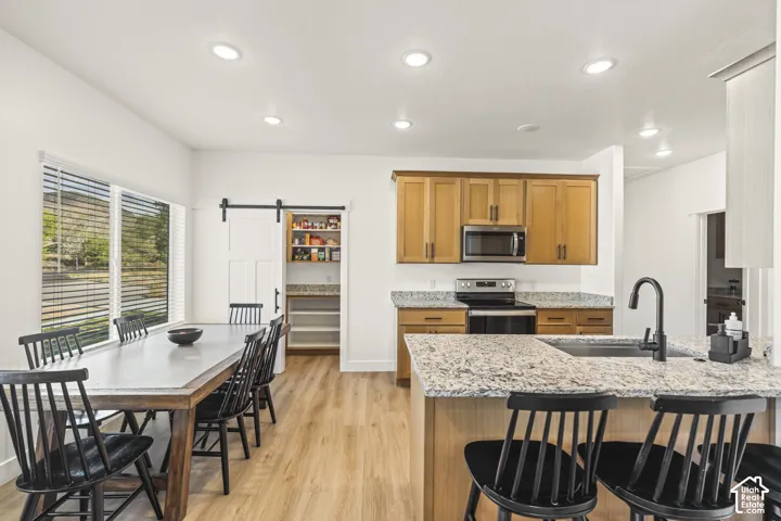 Kitchen featuring wood-finish cabinetry, stone-patterned countertops, recessed ceiling lighting, a walk-in pantry with a sliding barn-style door, and wood-finish flooring