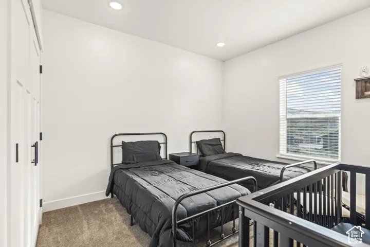 Neutral-toned carpeting, recessed ceiling lighting, a single-pane window with horizontal blinds, and a built-in closet with white paneled doors