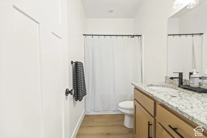Bathroom featuring a vanity with wood-finish cabinetry, a stone countertop with an integrated basin, matte black hardware, and wood-finish flooring