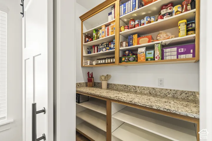 Pantry featuring custom wood cabinetry, stone-finish countertops, adjustable open shelving, and a white sliding door with matte black hardware