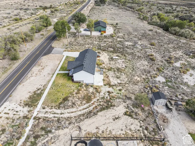 Aerial perspective of a property featuring a multi-structure lot, asphalt-shingle roofing, concrete walkways, a detached storage shed, and expansive acreage