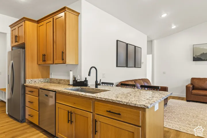 Kitchen featuring light wood cabinetry with matte black hardware, stone-patterned countertops, stainless steel appliances, and a matte black gooseneck faucet