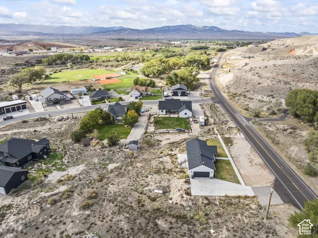 Aerial perspective featuring residential structures with dark gabled roofs, paved driveways, concrete walkways, and a mountainous horizon
