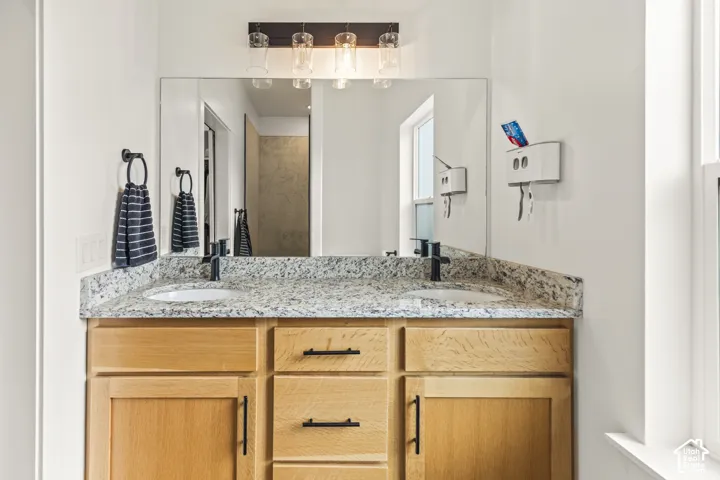 Dual-sink vanity featuring stone countertops, natural wood-finish cabinetry, matte black hardware, and an expansive wall-mounted mirror