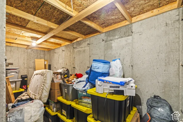 Storage area featuring exposed timber joist ceiling and poured concrete walls