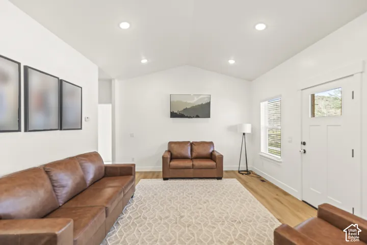 Vaulted ceiling, recessed lighting, and light-toned wood-finish flooring