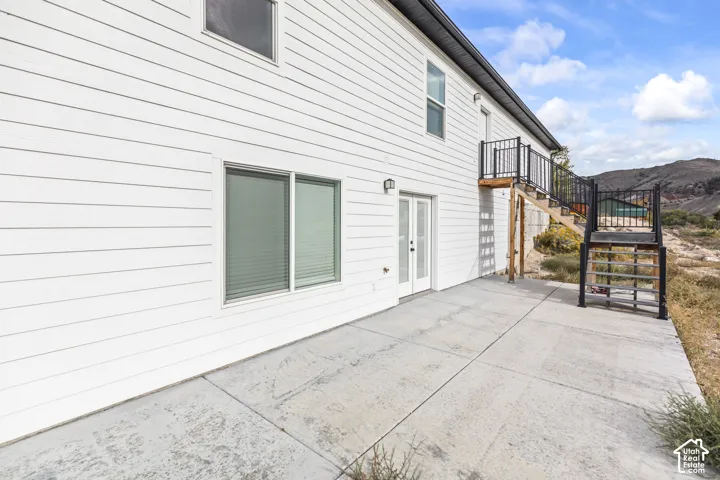 Exterior elevation featuring white horizontal siding, a concrete patio, double glass doors, and a metal staircase with railing