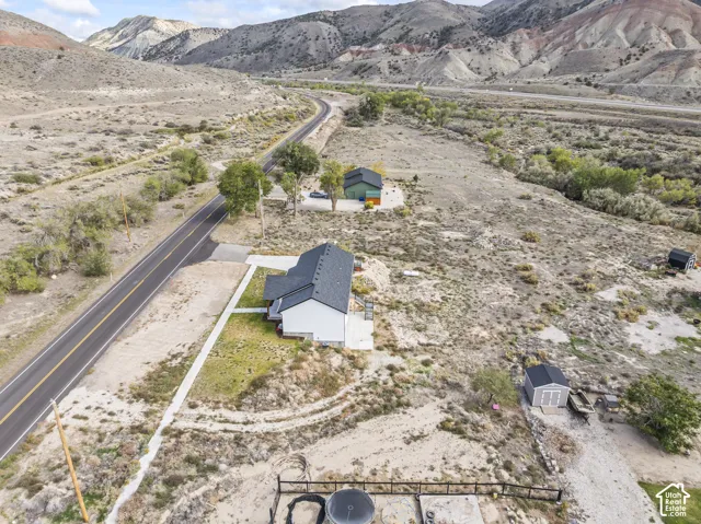 Aerial perspective of property featuring a multi-structure site, detached garage, storage building, concrete pathways, and surrounding mountain terrain