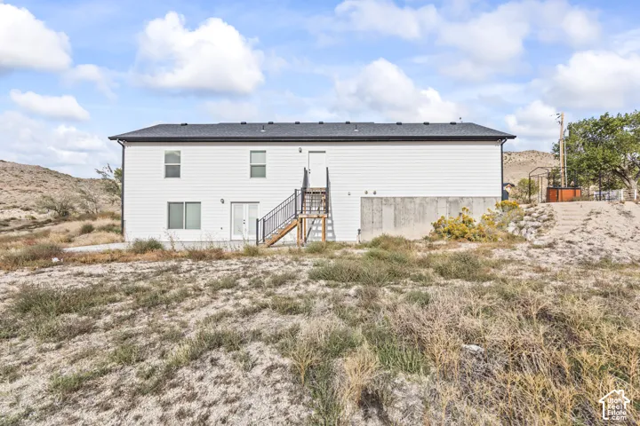 Exterior featuring white horizontal siding, a dark shingled roof, a raised metal staircase with railings, and a concrete foundation base set against a mountain landscape